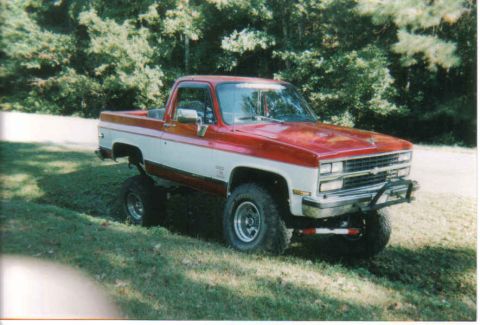 1974 Ford Bronco - This lifted pickup truck features a two-tone red and white paint scheme and prominent off-road tires.