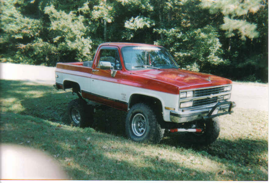 Red and white lifted pickup truck with chrome grille and off-road tires