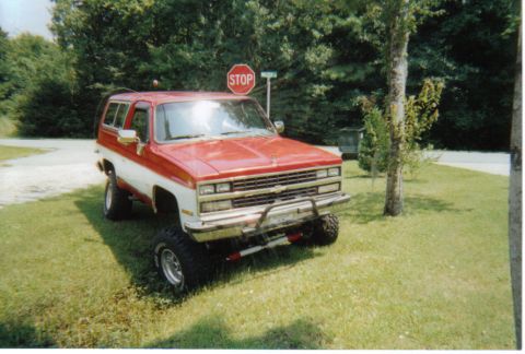1974 Ford Bronco - This lifted Chevrolet K5 Blazer is parked on a grassy area near a stop sign.