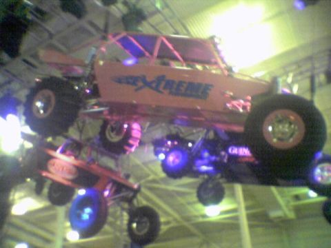 2005 BMW 3 Series - Multiple off-road vehicles are suspended indoors, with one prominent orange buggy displaying 'Xtreme' graphics.