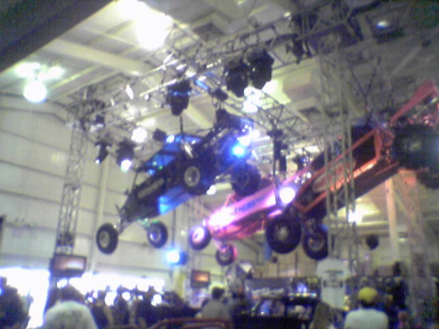 Blue and red off-road buggies displayed on overhead truss at an indoor auto expo