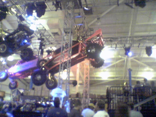 Red off-road vehicle suspended indoors, with another vehicle above it