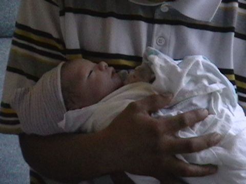 1997 Ford Probe - A person cradles a newborn baby, swaddled in white cloth and wearing a cap.