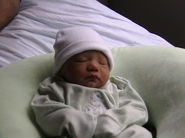 Baby wearing a white hat and light green onesie, sleeping in a green pillow