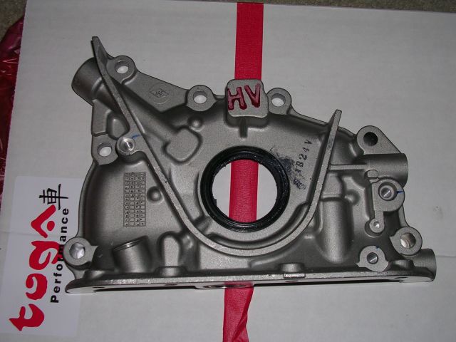 Metal oil pump with a red strap through it. Text on the side reads '1B24V'. A label on the left has Japanese characters and 'Performance'