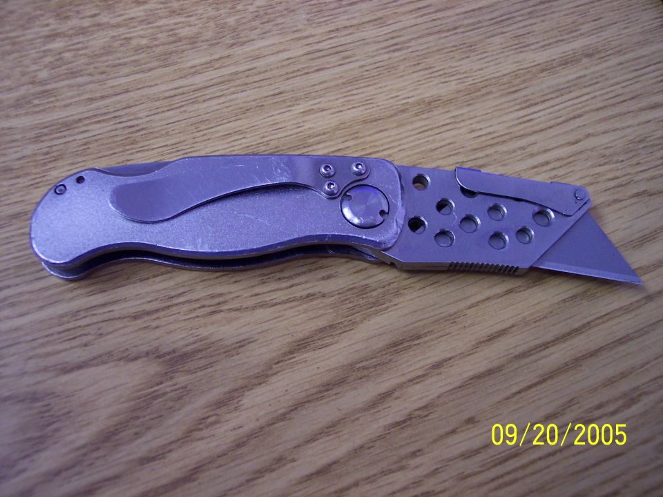 Utility knife with a silver handle and a retractable blade, lying on a wooden surface