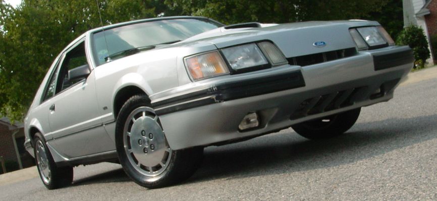 Silver coupe parked on a street, front quarter view. Hood scoop visible