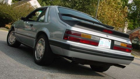 1986 Ford Mustang - A silver 1986 Ford Mustang is parked on a street, viewed from the rear quarter angle.