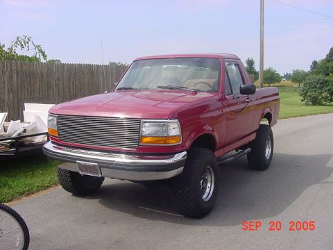 1989 Ford Bronco - This red pickup truck features a prominent chrome grille and lifted suspension, suggesting a model year around 1992.
