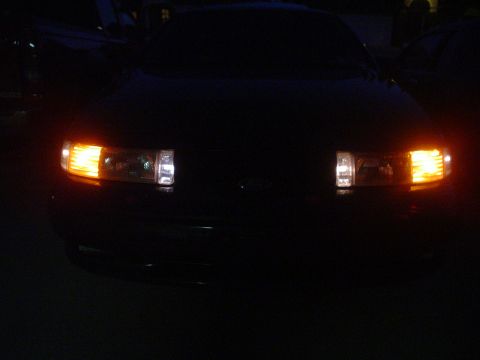 1993 Ford Taurus - Front view of a black Ford Taurus with illuminated headlights and amber turn signals in the dark.