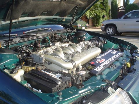 1993 Ford Taurus - The engine bay of a green vehicle is open, revealing the V6 engine and a plaque from AGILITYMOTORSPORTS.COM. Other vehicles are visible in…