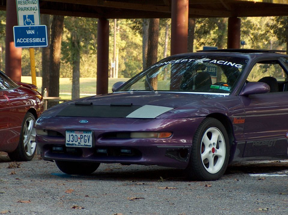 Purple 1996 Ford Probe GT with white wheels and a black car cover on the hood, parked next to a red car