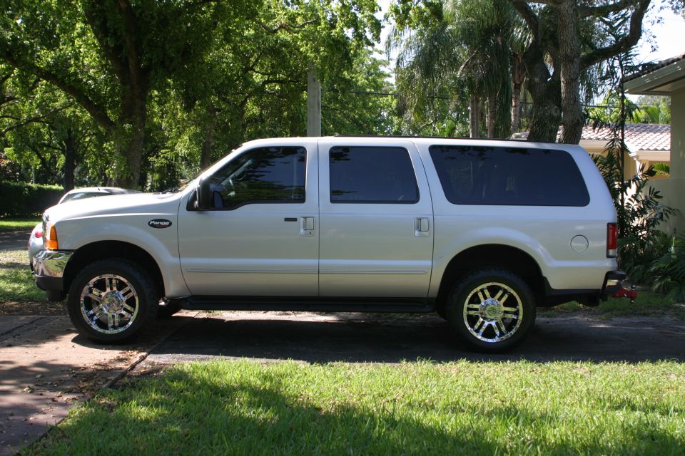 Silver-beige Ford Excursion SUV in profile in a shaded driveway on chrome wheels