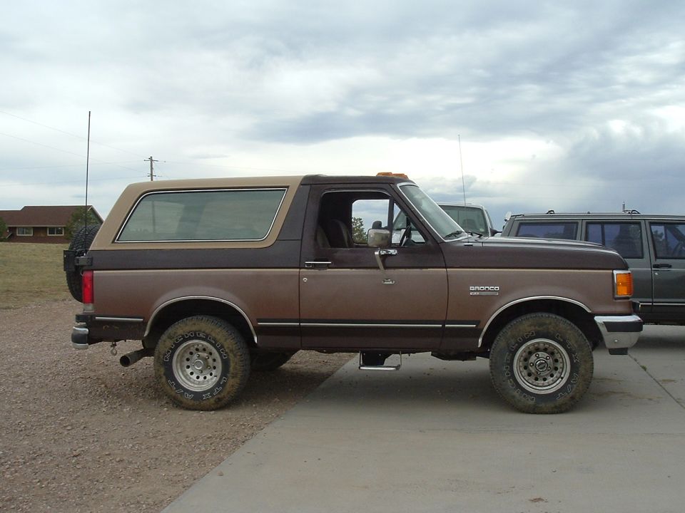 Brown two-tone 1980s Ford Bronco parked on a driveway under overcast sky