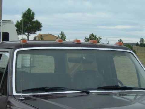 1989 Ford Bronco - The top of a truck's cab is shown, several orange clearance lights against a cloudy sky.