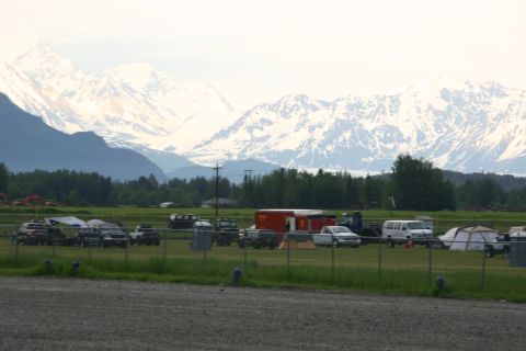 2003 Jeep TJ - A collection of vehicles are parked in a grassy field with a large mountain range visible behind them.