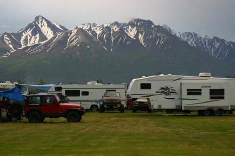 2003 Jeep TJ - A red Jeep Wrangler is parked on a grassy field with RVs and snow-capped mountains in the background.