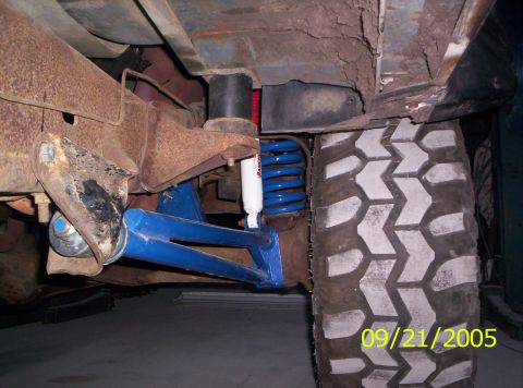 1985 Ford Bronco - Close-up of the undercarriage, showing blue suspension components, a Rancho shock absorber, and a large off-road tire.