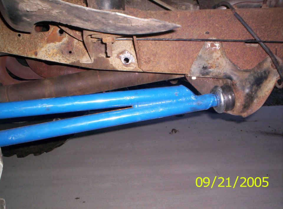 Close-up of blue suspension arm attached to rusty frame with exhaust pipe visible
