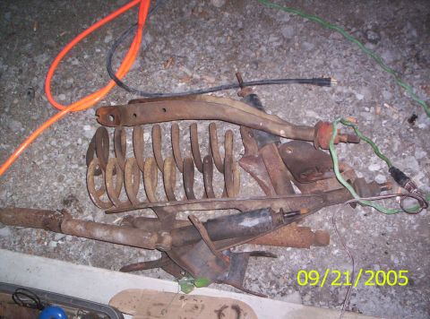 1985 Ford Bronco - Various rusty vehicle suspension components are laid out on a concrete surface, accompanied by electrical cords.