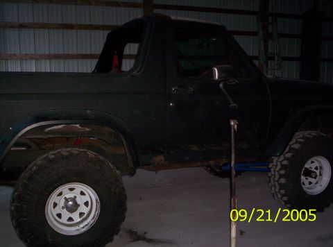 1985 Ford Bronco - A black Ford Bronco with a lifted suspension and large tires is parked indoors, showing its side profile.
