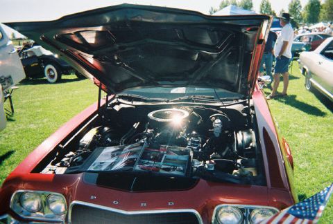 1972 Ford Ranchero - A red 1972 Ford Ranchero is displayed with its hood open, revealing the engine and promotional materials on the engine bay.