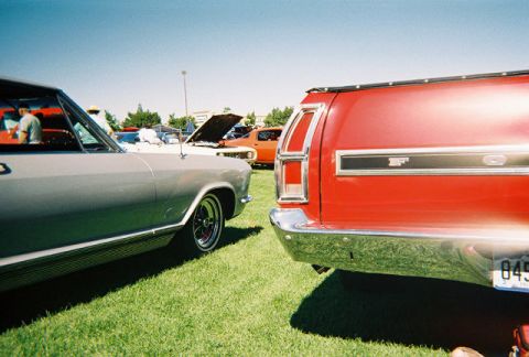 1972 Ford Ranchero - A red 1972 Ford Ranchero is parked next to a grey car on a grassy field under a clear blue sky.