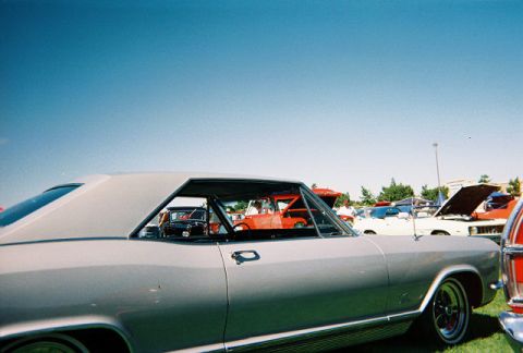 1972 Ford Ranchero - A silver coupe, likely a 1965 model, is parked on grass with other vehicles visible under a clear blue sky.