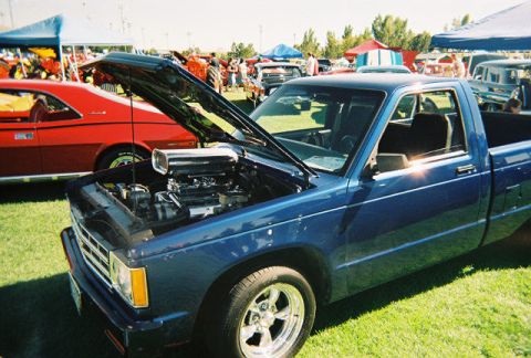 1972 Ford Ranchero - A blue pickup truck is parked on grass with its hood open, revealing a large engine component. Another car is visible behind it.
