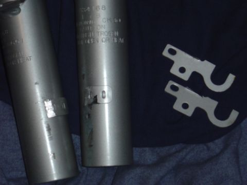 1998 Ford Taurus - Close-up of two cylindrical metal parts and two U-shaped metal brackets.