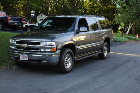 2001 Ford Crown Victoria - Gray 2002 Chevrolet Suburban parked in a residential driveway with trees and houses visible.