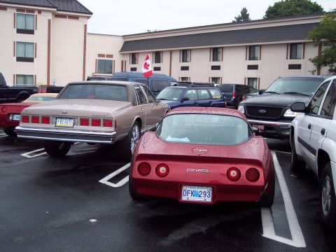 2001 Ford Crown Victoria - A red Chevrolet Corvette is parked in a lot next to other vehicles, with a Canadian flag in the background.