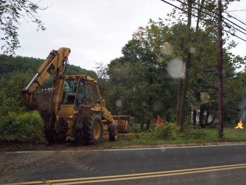 2001 Ford Crown Victoria - A yellow backhoe loader is parked on the side of a road, with a fire visible in the distance.