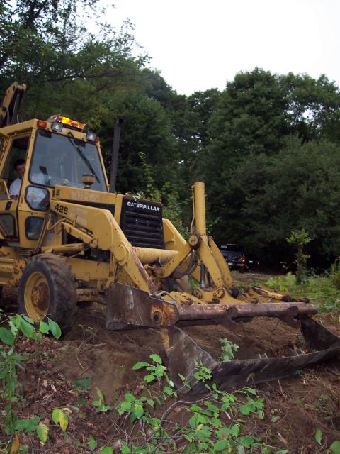 2001 Ford Crown Victoria - A yellow Caterpillar backhoe loader is seen in operation, digging into a dirt mound.