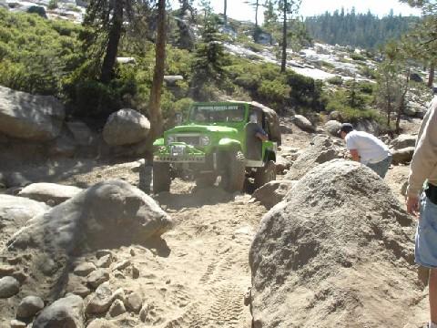 1996 Ford Bronco - A green off-road vehicle is shown traversing a challenging, rocky terrain on a sunny day.