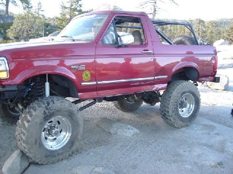 1996 Ford Bronco - A red 1996 Ford Bronco is shown with off-road modifications in a rocky, outdoor setting.