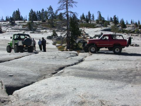 1996 Ford Bronco - A red 1996 Ford Bronco is parked on a rocky terrain, with a green Jeep and people in the background.