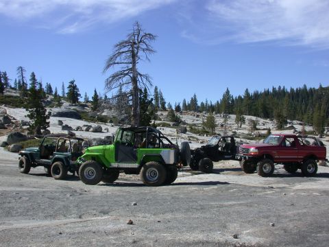 1996 Ford Bronco - Four off-road vehicles, including a 1996 Ford Bronco, are parked on a rocky, wooded hillside.