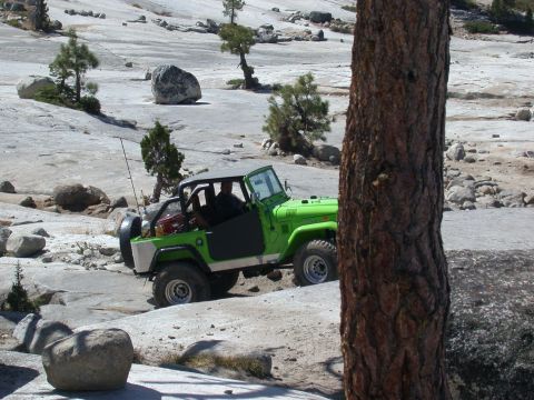 1996 Ford Bronco - A green off-road vehicle navigates a rocky terrain on a sunny day.