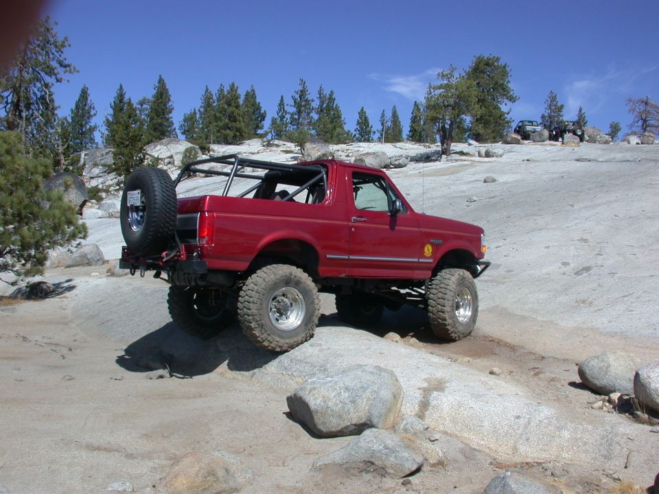 Red 1996 Ford Bronco off-roading on rocks with a spare tire mounted on the rear