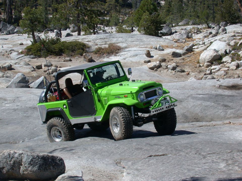 Green Toyota Land Cruiser FJ40 with aftermarket bumper and roll cage driving on rocky terrain