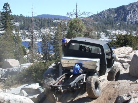 1996 Ford Bronco - This modified pickup truck navigates a rocky trail with a scenic lake and mountains in the background.
