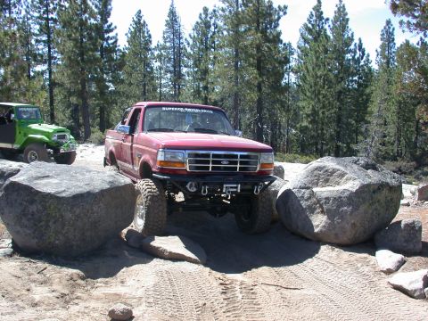 1996 Ford Bronco - Red Ford F-Series truck and green Jeep tackle rocky terrain on an off-road trail.