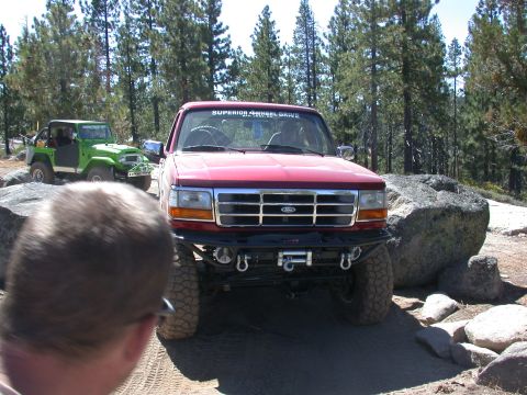 1996 Ford Bronco - A red 1996 Ford Bronco is parked off-road with a green Jeep in the background.