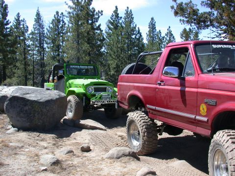 1996 Ford Bronco - Two modified off-road vehicles navigate a challenging rocky terrain on a sunny day.