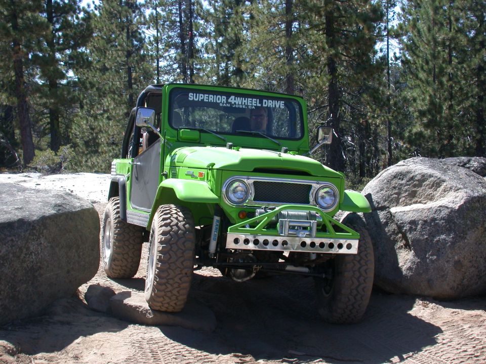 Green off-road SUV with a winch on the front bumper, navigating between large rocks on a dirt trail