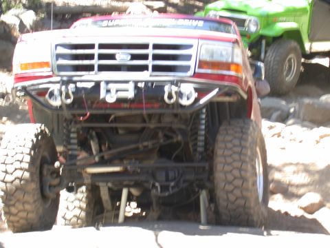 1996 Ford Bronco - A modified red Ford Bronco navigates rocky terrain, with a green Jeep visible in the background.