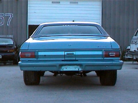 1977 Ford F-150 - Rear view of a blue sedan with wide tires, parked in front of a garage door.