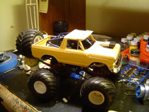 1979 Ford Bronco - A yellow 1979 Ford Bronco model is shown mid-build, oversized monster truck tires and a roll cage.
