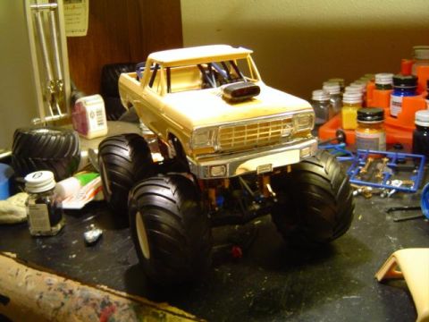 1979 Ford Bronco - A model truck with oversized tires and a prominent hood scoop is displayed on a cluttered workbench.